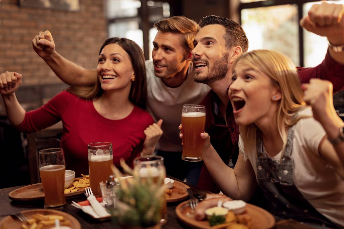 Group of friends in a sports club celebrating with food and drink.