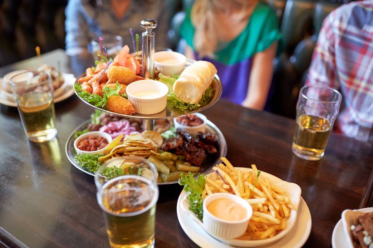 People sitting at table with food and beer at bar.